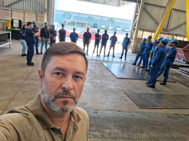 Trabalhadores uniformizados em fila dentro de um galpão industrial, durante o diálogo de segurança.