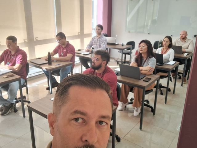 Turma em sala de aula com carteiras; em primeiro plano, o instrutor.